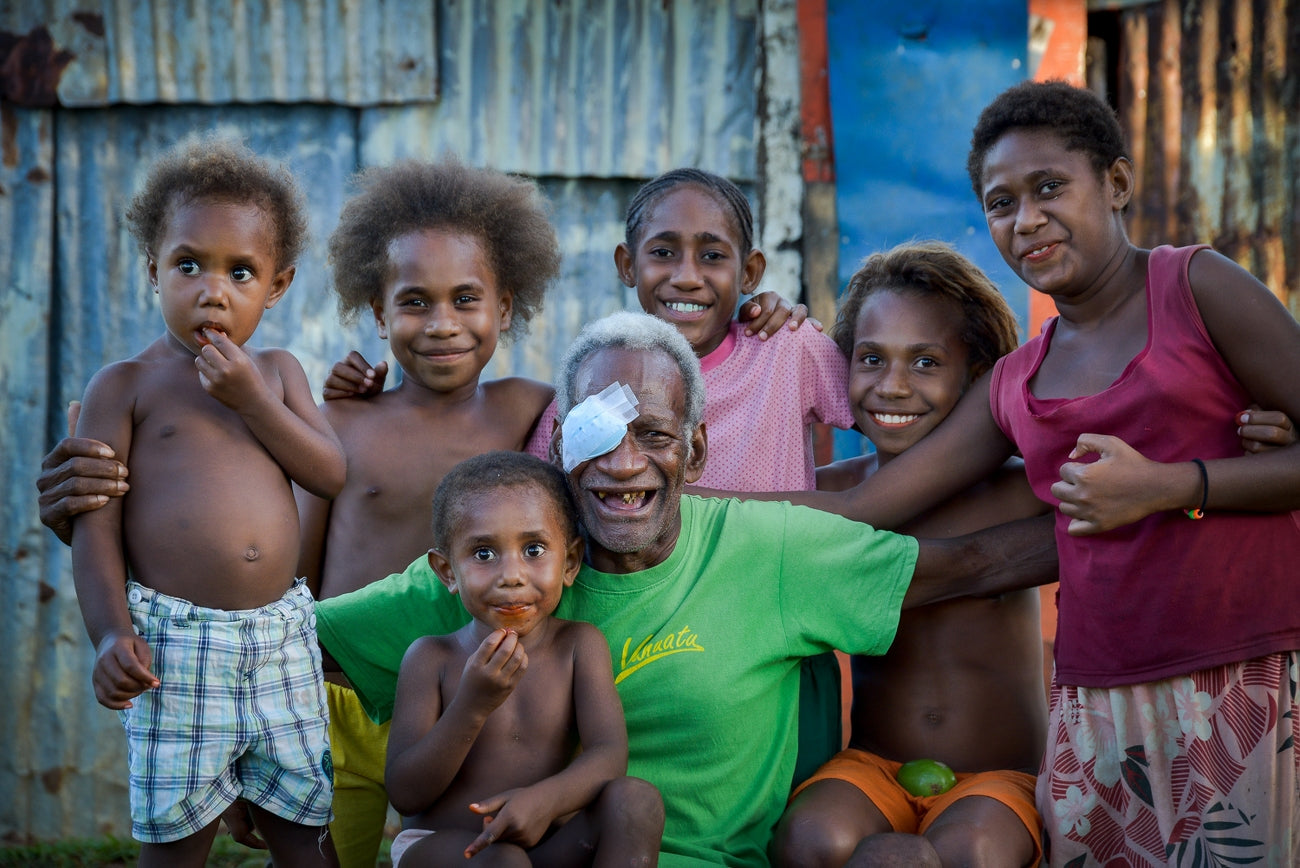 Pacific Island man with eye patch, smiling with children after restoring eyesight.